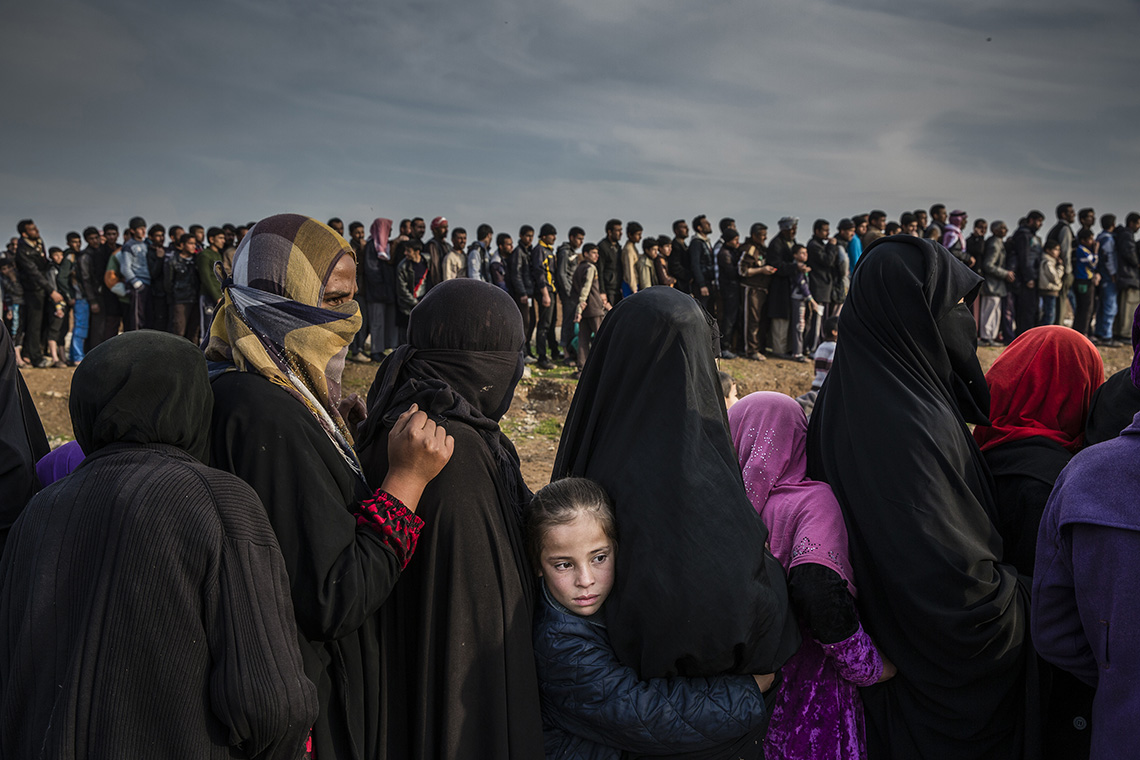 Civilians who had remained in west Mosul after the battle to take the city line up for aid in the Mamun neighbourhood. One girl turns her face to the masses while the others look on. Shot by Ivor Prickett.  